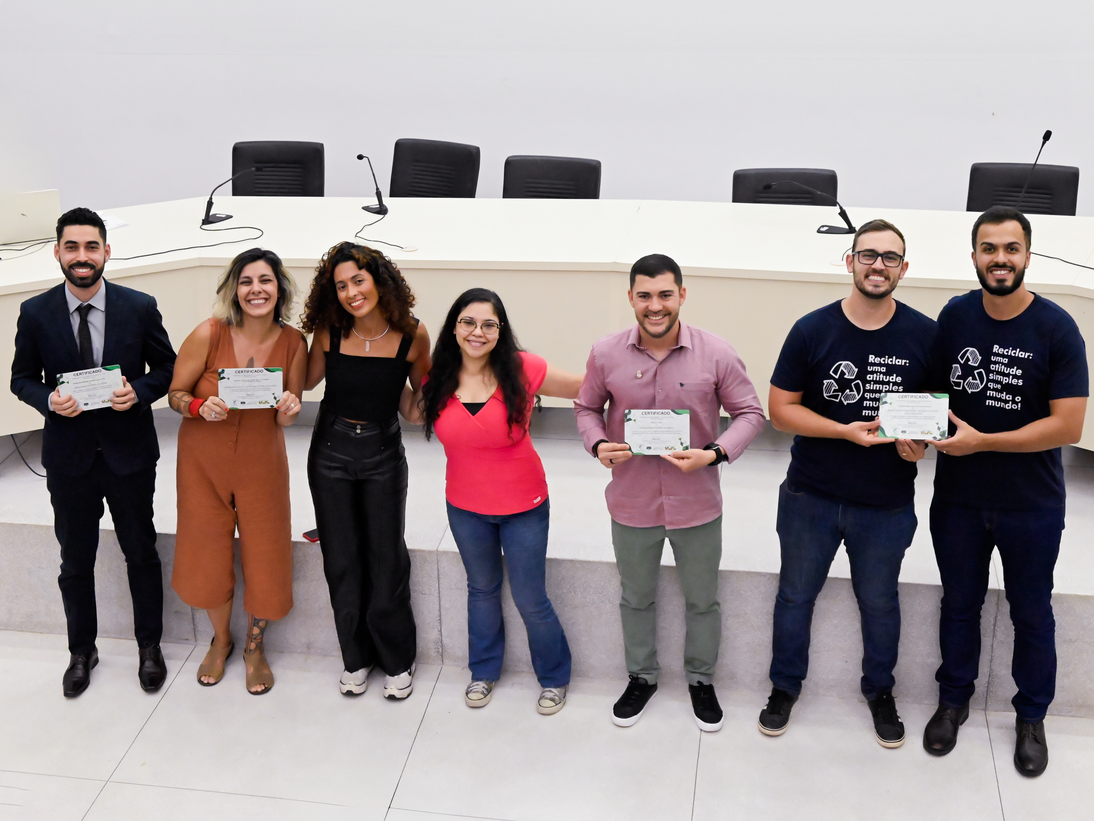 4 homens e 3 mulheres jovens vistos de cima, olhando para nós e sorrindo, com certificado em mãos.  