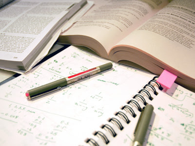 Imagem ilustrativa: canetas de tampa verde sobre um caderno abeto co fórmulas de matemática anotadas. 