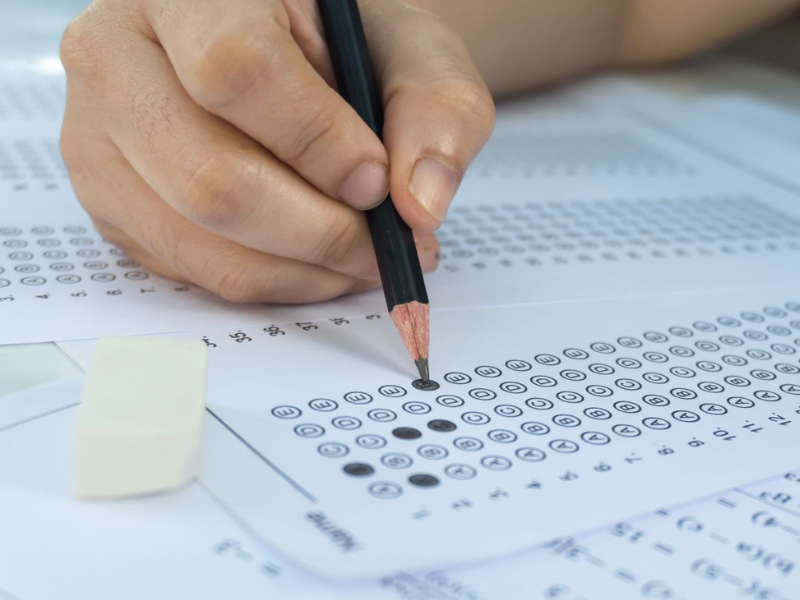 Mão de pessoa branca segurando um lápis e marcando uma resposta em um gabarito. 