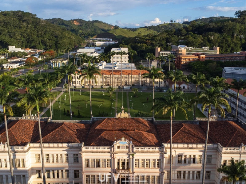 Foto aérea mostra o prédio principal da UFV e o alojamento velho, ambos bege com altas janelas de madeira. 
