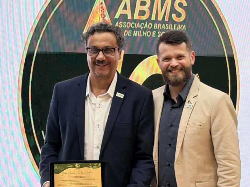João Carlos (branco idoso) e homem jovem desconhecido (branco de barba castanha) lado a lado para a foto. 