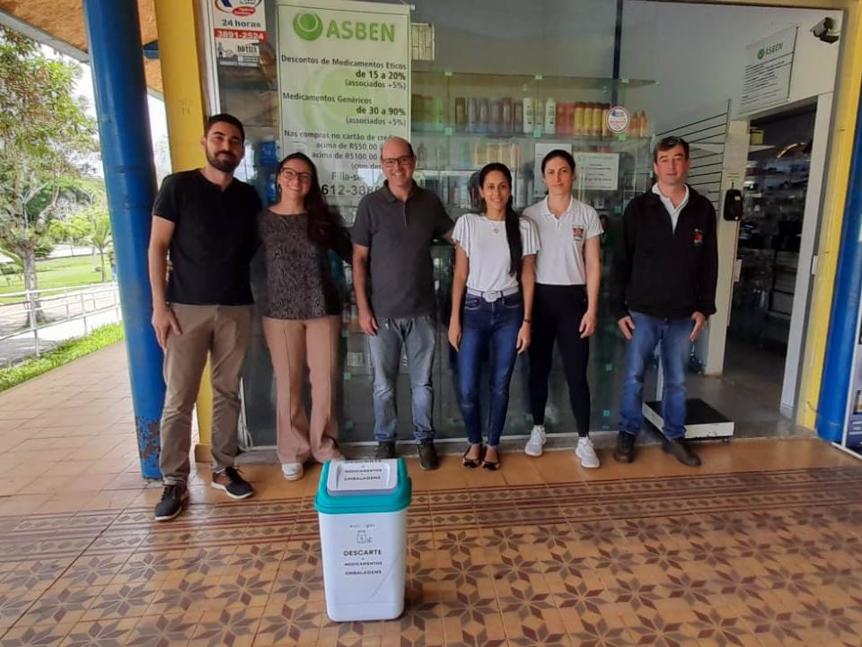 Membros da Asben e da Diretoria de Meio Ambiente em frente à farmácia da Asben. À frente, lixeira especial para descarte. 