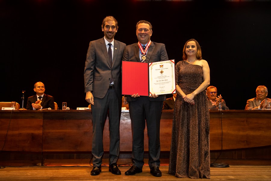 André Souto Maior Pessôa recebe a medalha de honra ao mérito e posa para foto com o reitor Demetrius e a vice-reitora Rejane.