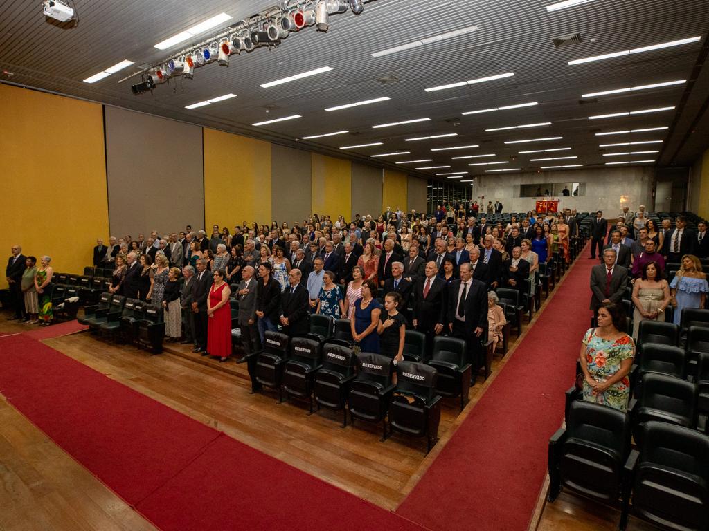 Auditório do Espaço Fernando Sabino lotado. Todos estão de pé durante a execução do Hino Nacional. 