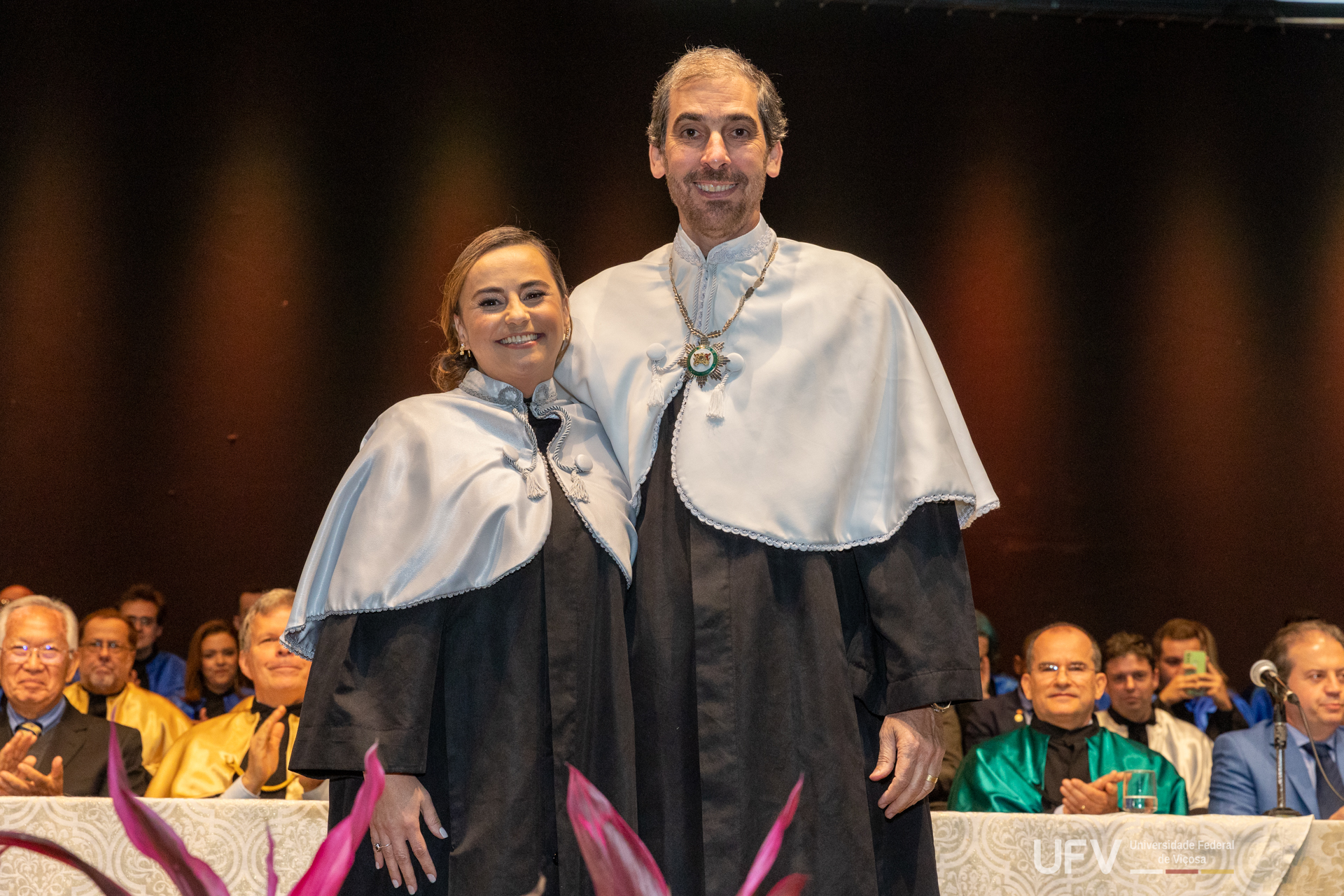 Rejane e Demetrius posam para foto, ambos vestindo a indumentária cerimonial, durante os aplausos das autoridades. 