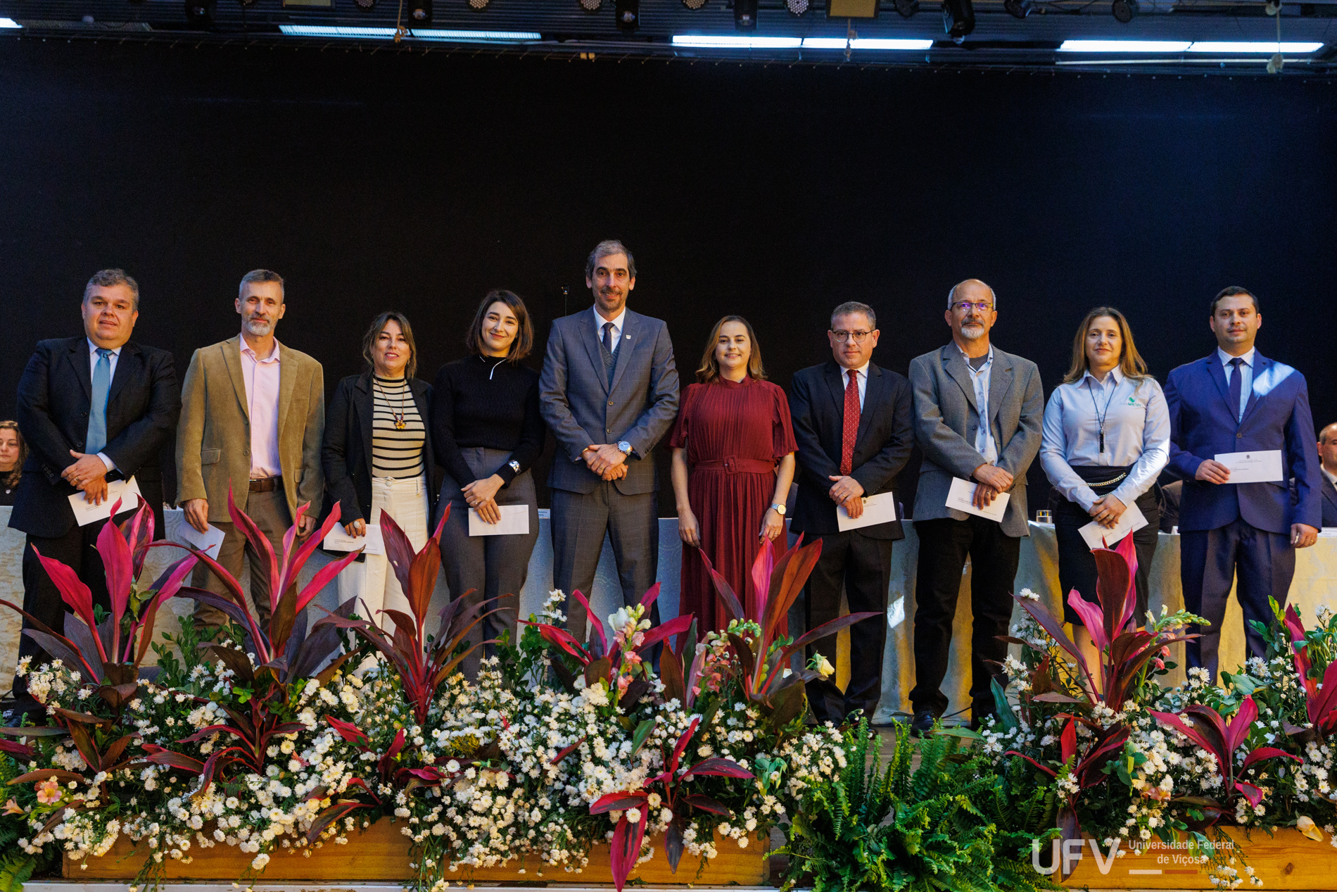 Demetrius, Rejane, pró-reitores e demais autoridades lado a lado para a foto, atrás do arranjo de flores do palco. 