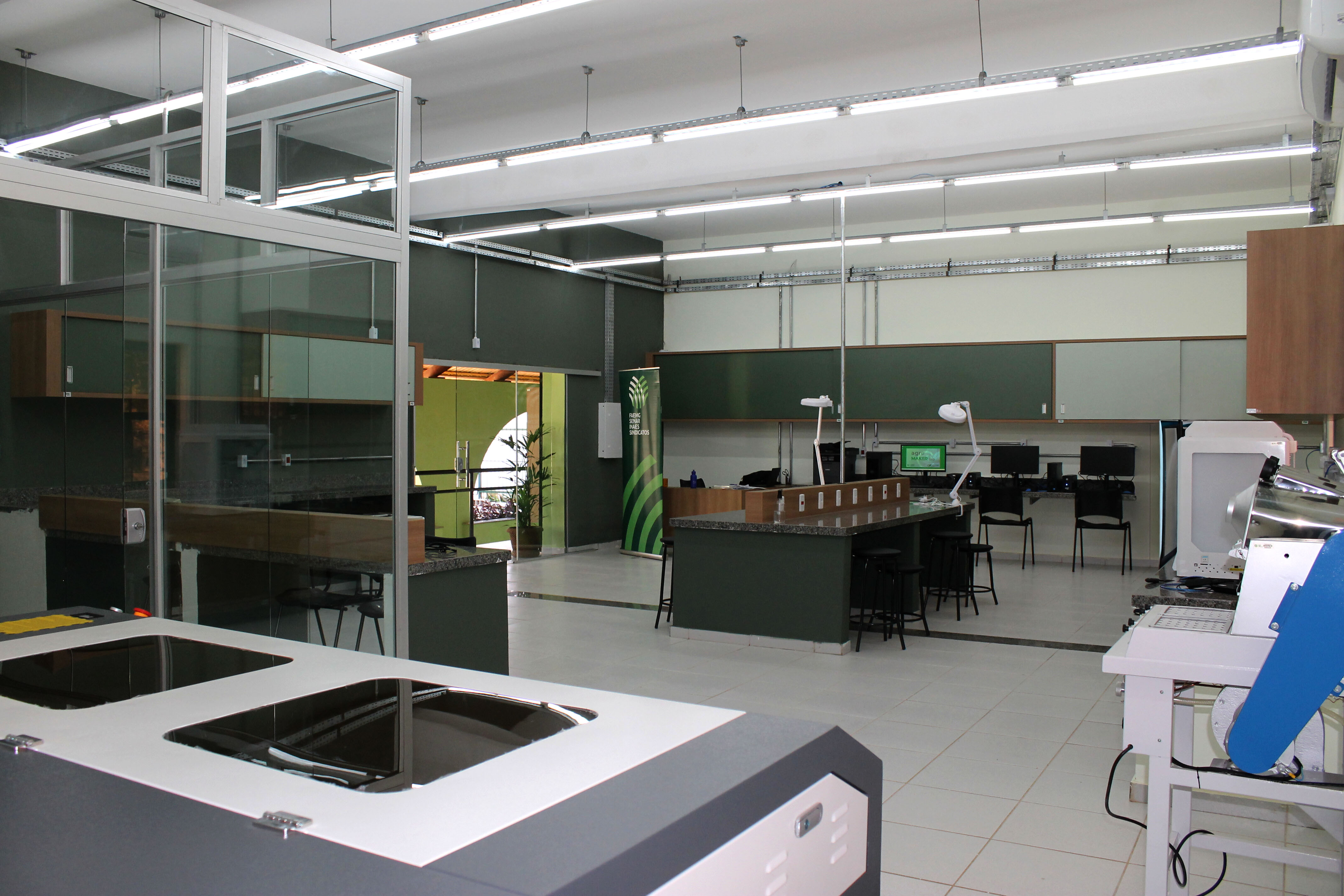 Foto de um laboratório de piso branco e paredes verde escuras, com bancada e cadeiras pretas. 