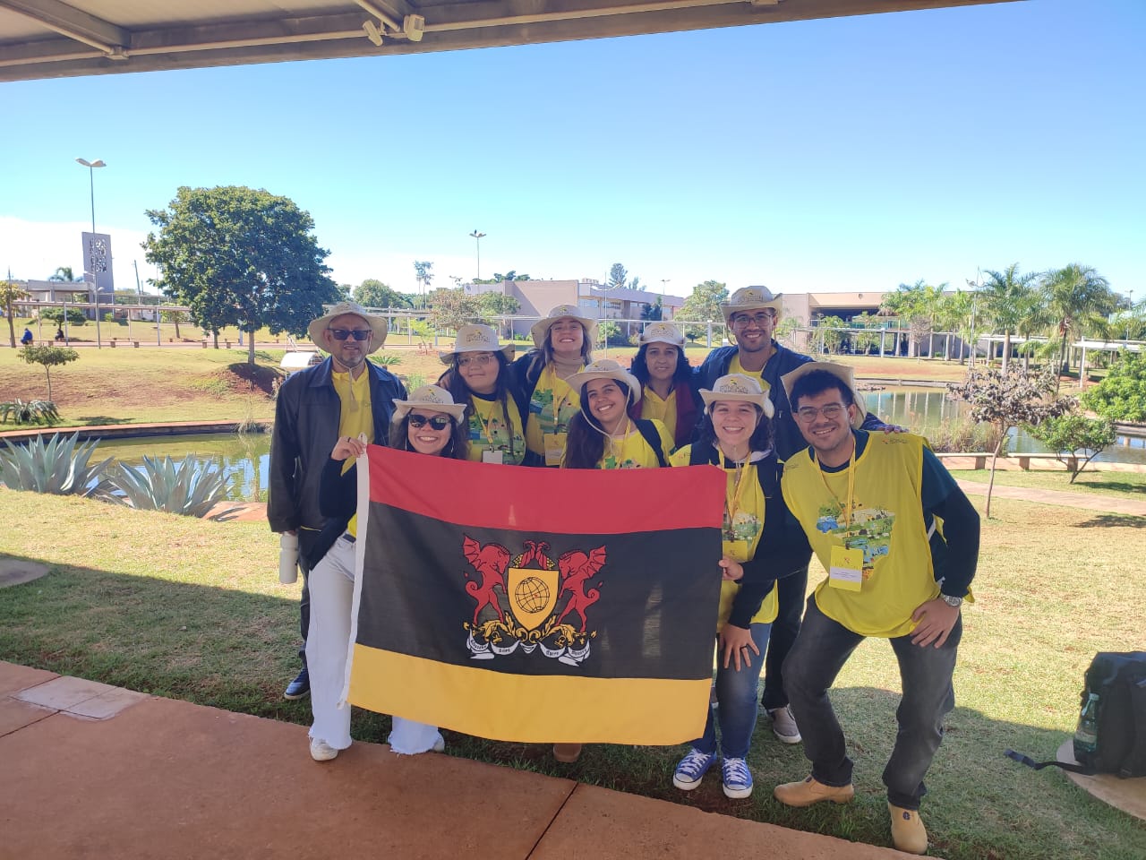 Foto da equipe posando para foto segurando uma bandeira com o brasão da UFV. Todos estão de preto e coletes amarelos. 