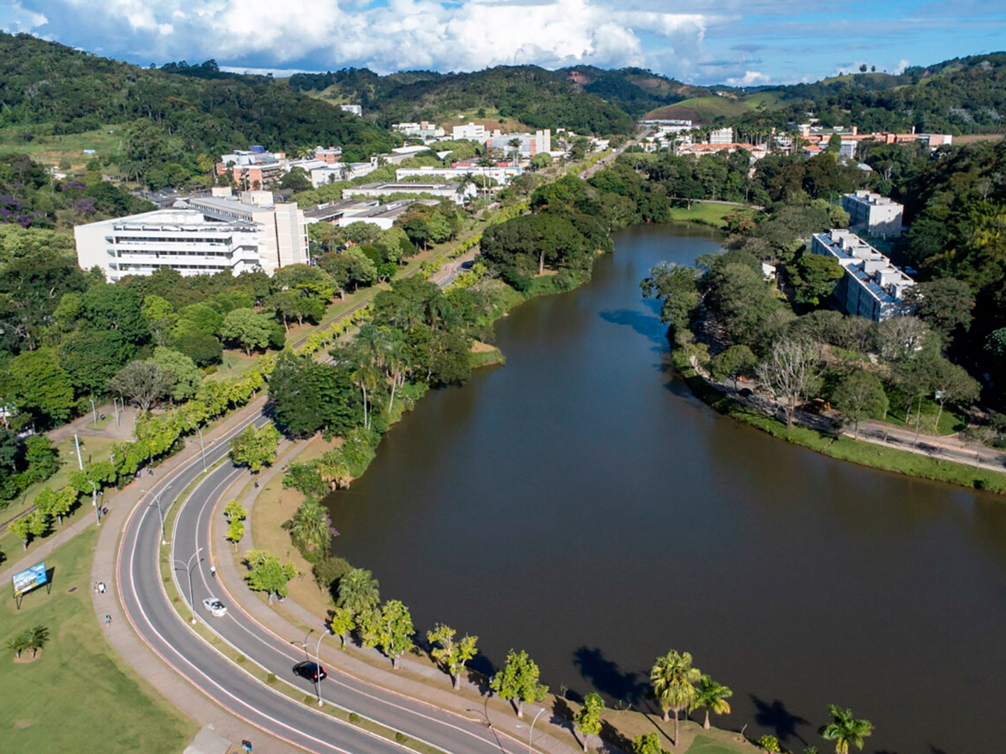 Foto aérea de uma grande lagoa contornada por uma longa rua com canteiro central e muitas árvores de ambos os lados. 