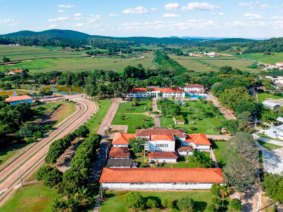 Foto áerea de longos casarões de 2 andares e telhas de barro circundados por muitas árvores e áreas verdes. 