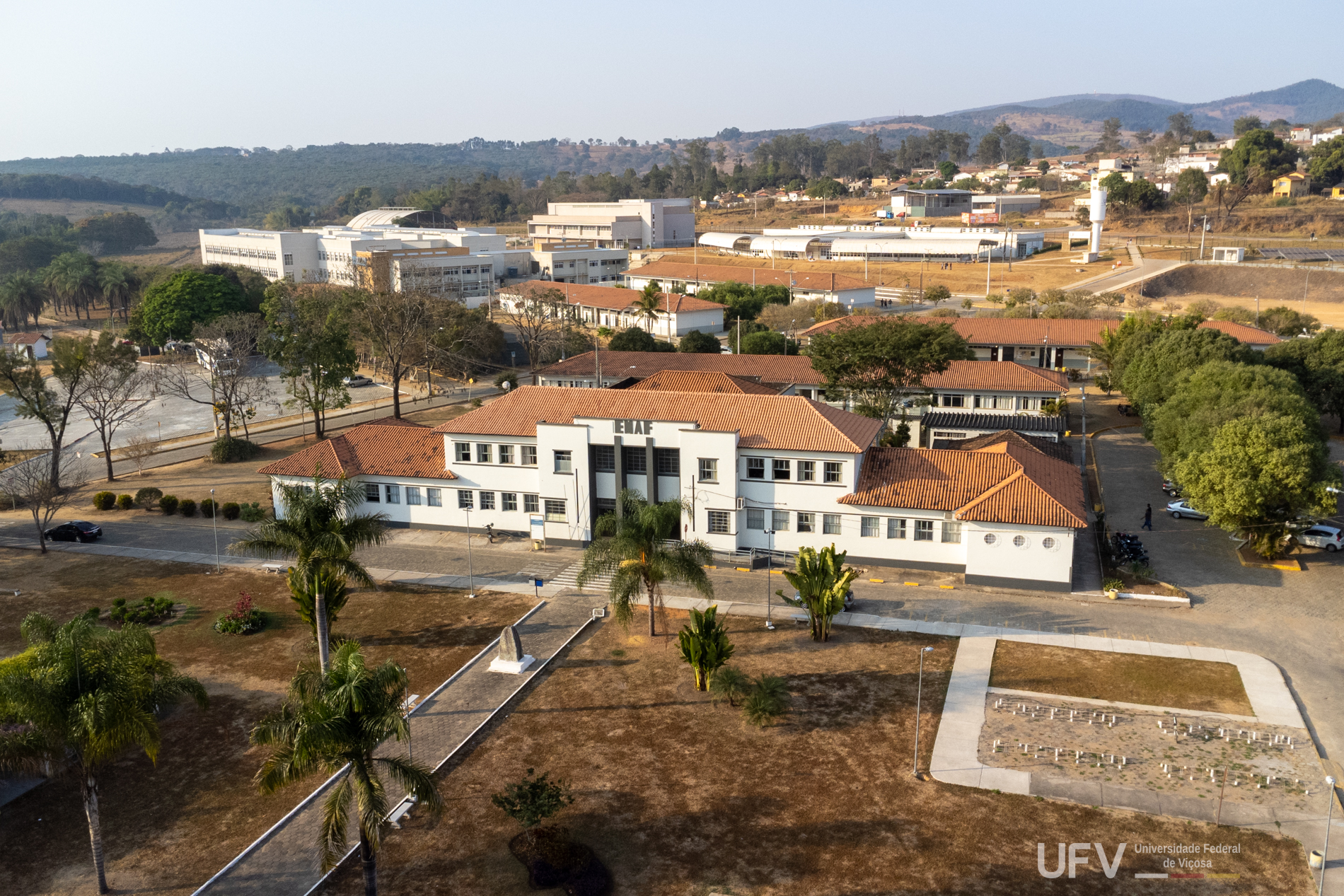 Foto aérea mostra um grande casarão branco com telha de barro e vários prédios baixos mais ao fundo da foto. 