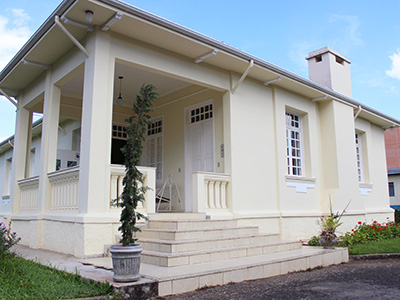 Fachada de uma casa branca de arquitetura antiga, com janelas e portas brancas e altas, e uma pequena chaminé. 