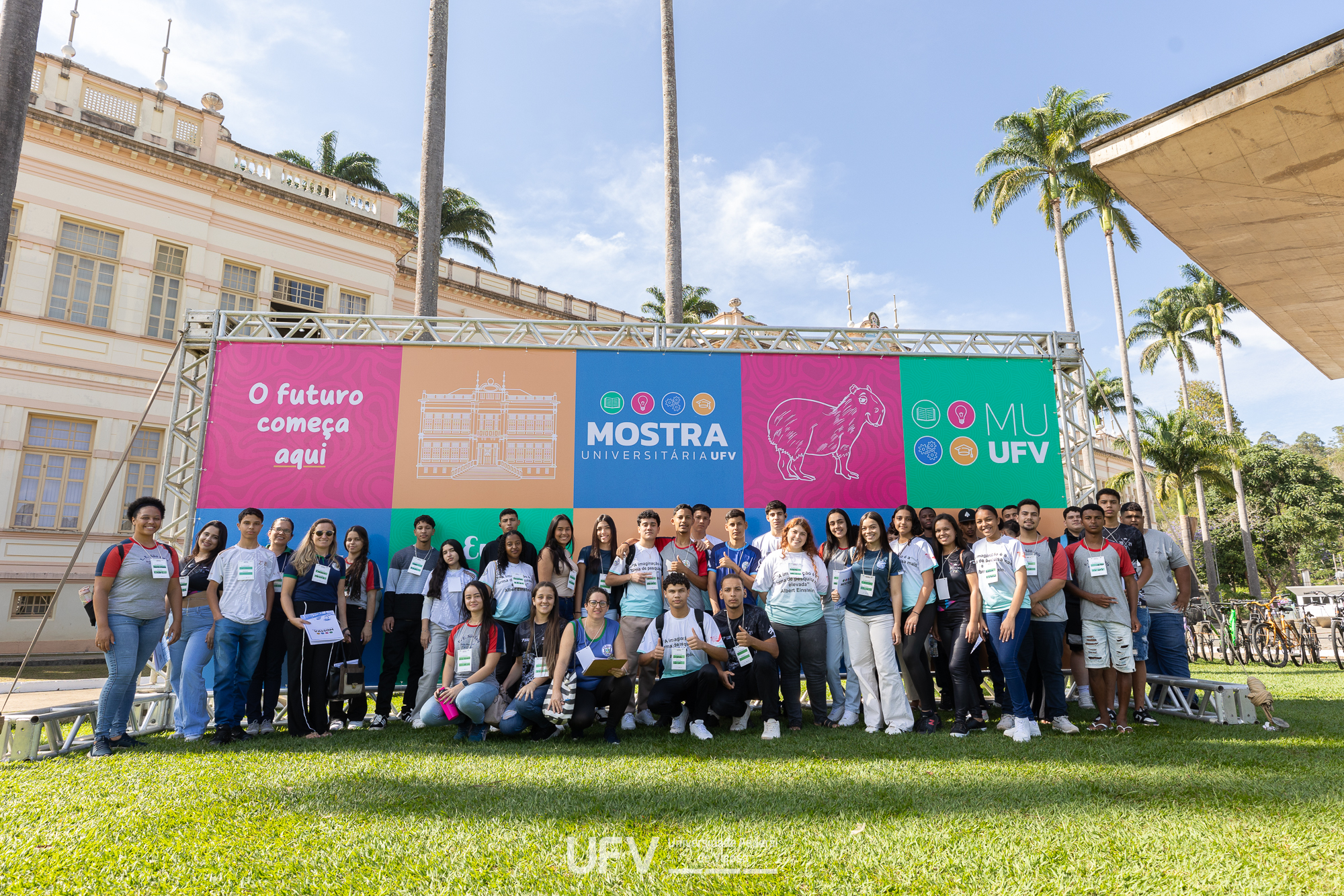 Dezenas de jovens posam em frente a um painel multicolorido da Mostra Universitária. 