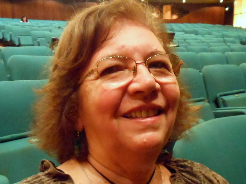 Elisa: mulher idosa, branca, loira, cabelos lisos na altura dos ombros, nariz largo, óculos corretivo. Ela sorri na foto. 