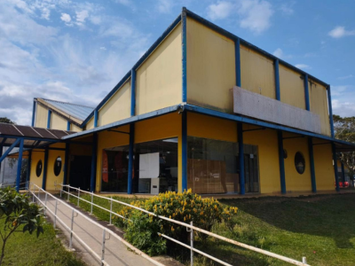 Prédio amarelo com telhado azul em forma de V, com colunas finas azuis e janelas redondas. 